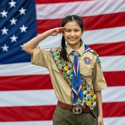 Eagle scout wearing a merit badge sash saluting in front of an American flag